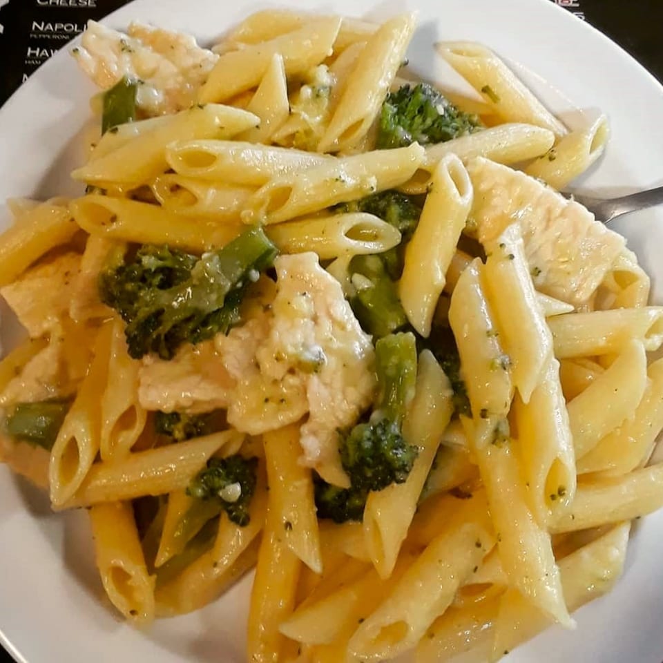 Penne pasta with creamy sauce, chicken, and broccoli florets on a white plate.