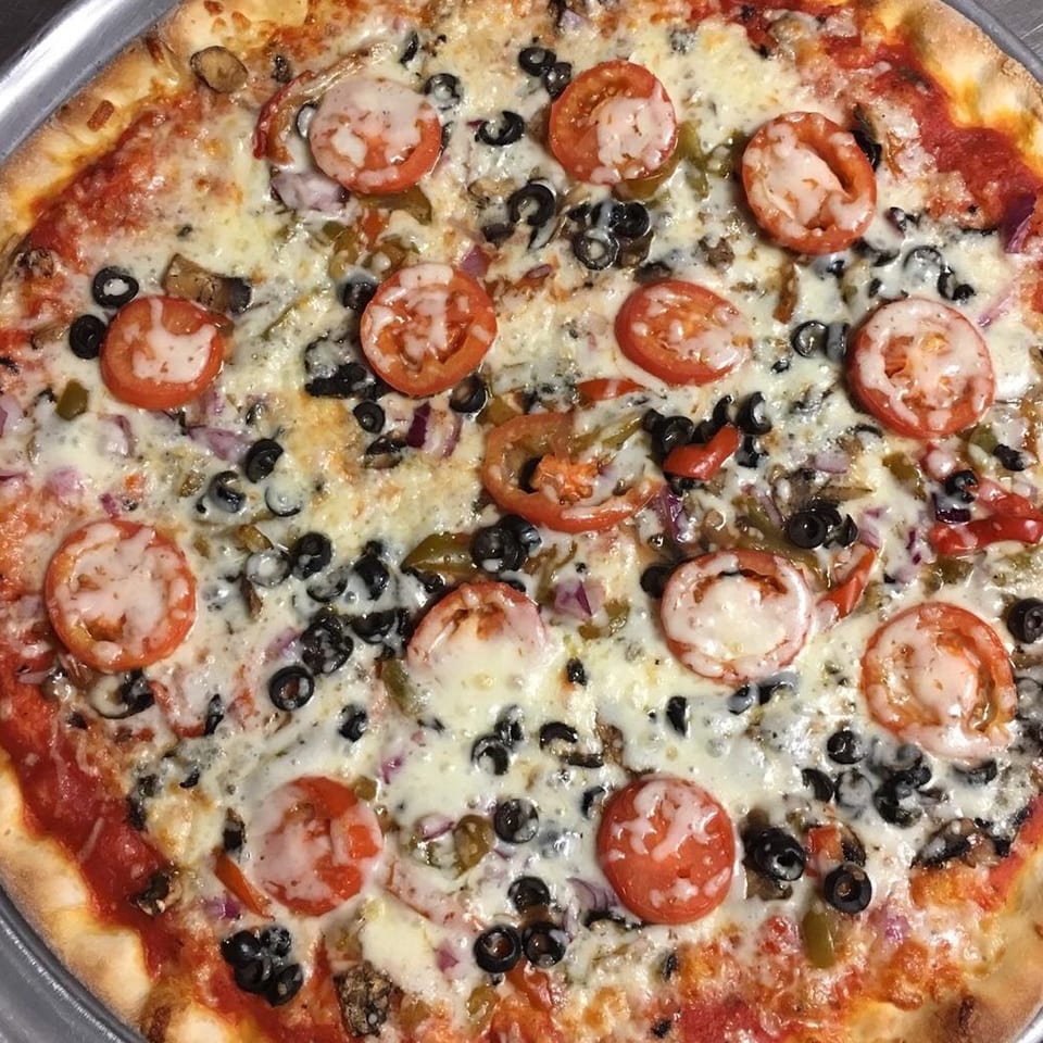 A Napoli's Pizzeria pizza with melted cheese, sliced tomatoes, black olives, and other vegetables.