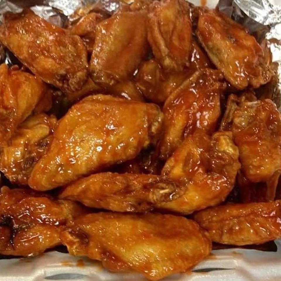 Close-up of a pile of glistening, saucy chicken wings in a foil-lined container from Napoli's Pizzeria.